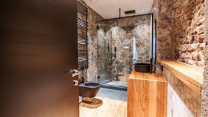 Une salle de bain moderne avec un mur en pierre, un meuble-lavabo en bois et une cabine de douche en verre.