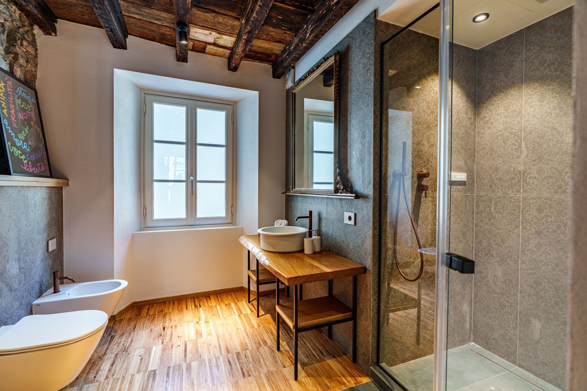 A bathroom with a wooden floor, a white bathtub, a toilet, a sink with a mirror, and a glass shower enclosure.