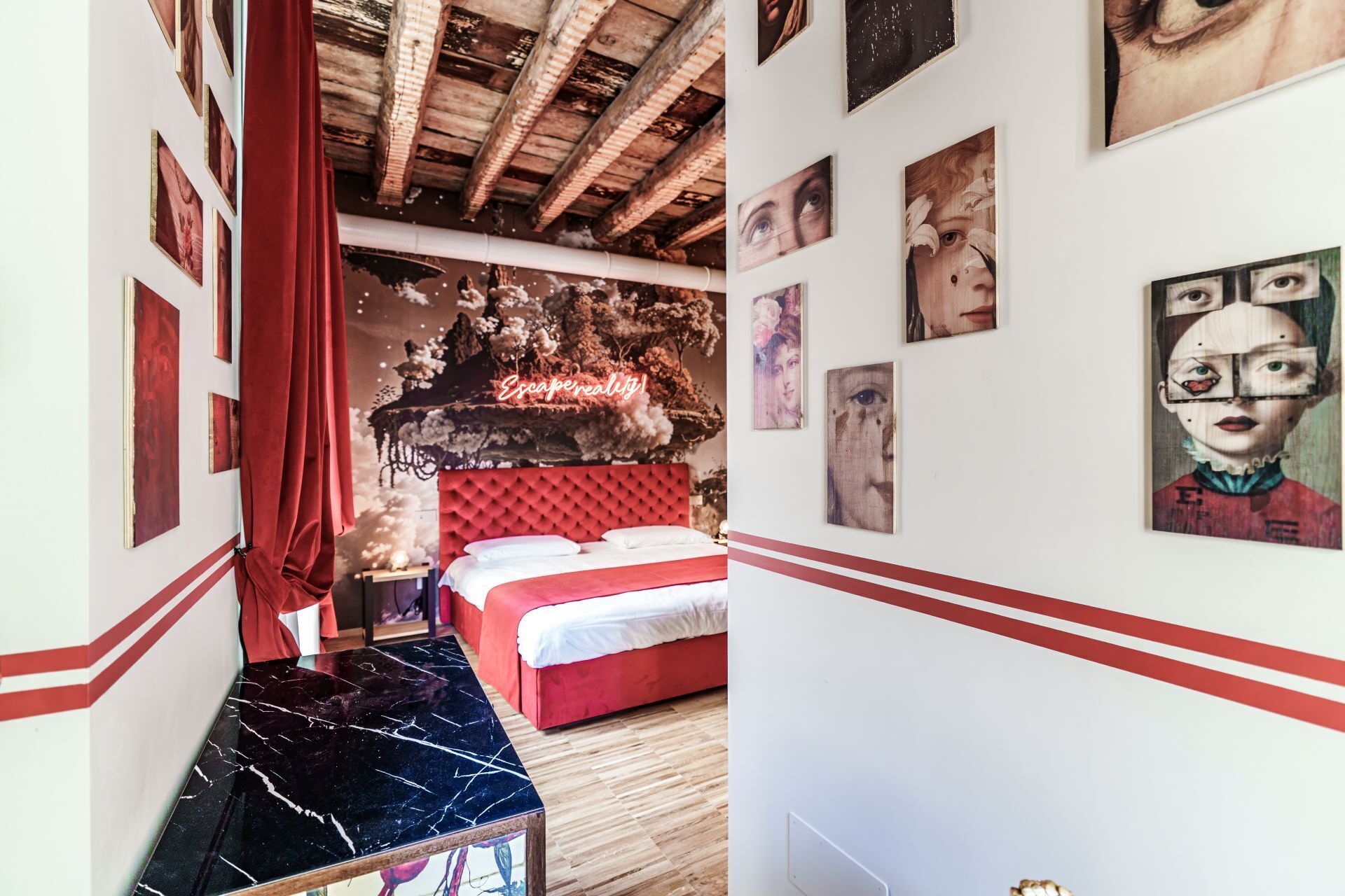 A bedroom with a red bed, a marble coffee table, and artwork on the walls.