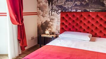 A bedroom with a red tufted headboard, a white bedspread, and a wall mural of clouds.