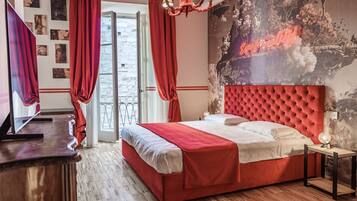 A bedroom with a red bed, a television, a chandelier, and a mural on the wall.