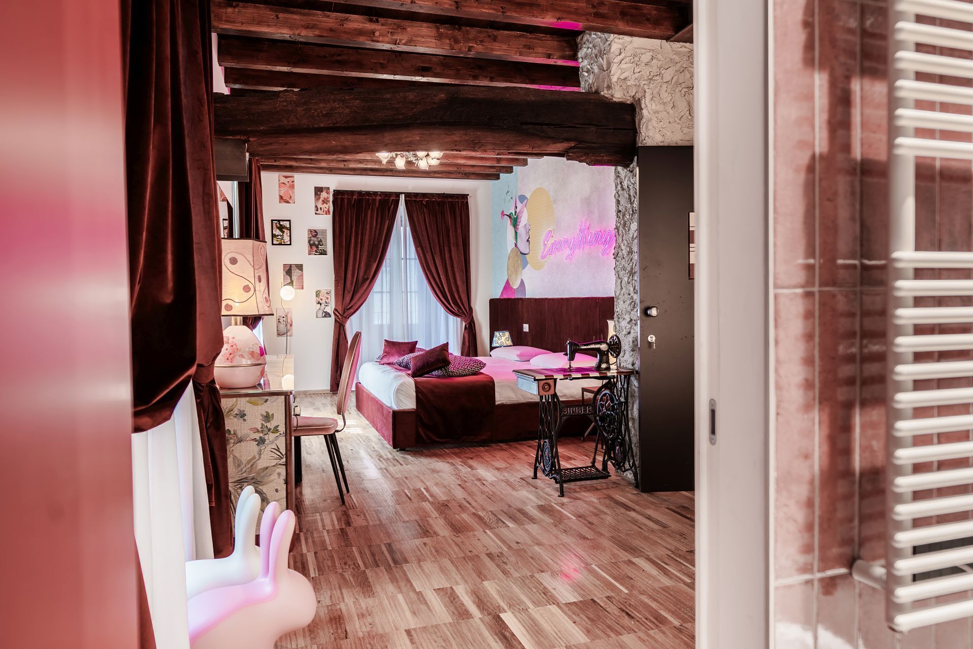 A bedroom with a wooden floor, a bed with a headboard, a sewing machine, and a wall with a colorful mural.