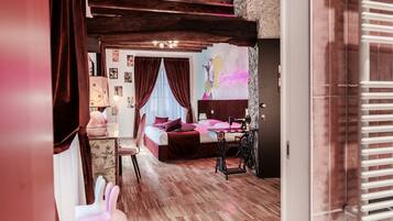 A bedroom with a wooden floor, a bed with a headboard, a sewing machine, and a wall with a colorful mural.