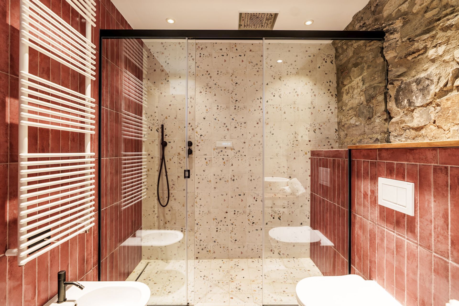 Un baño moderno con cabina de ducha de vidrio, dos lavamanos y pared de piedra.