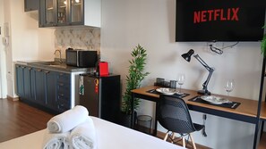 A modern kitchen with a microwave, a small refrigerator, and a sink. There is a dining area with a table, chairs, and a TV displaying 'NETFLIX'. - Vista incrível com AC e academia (São Paulo)