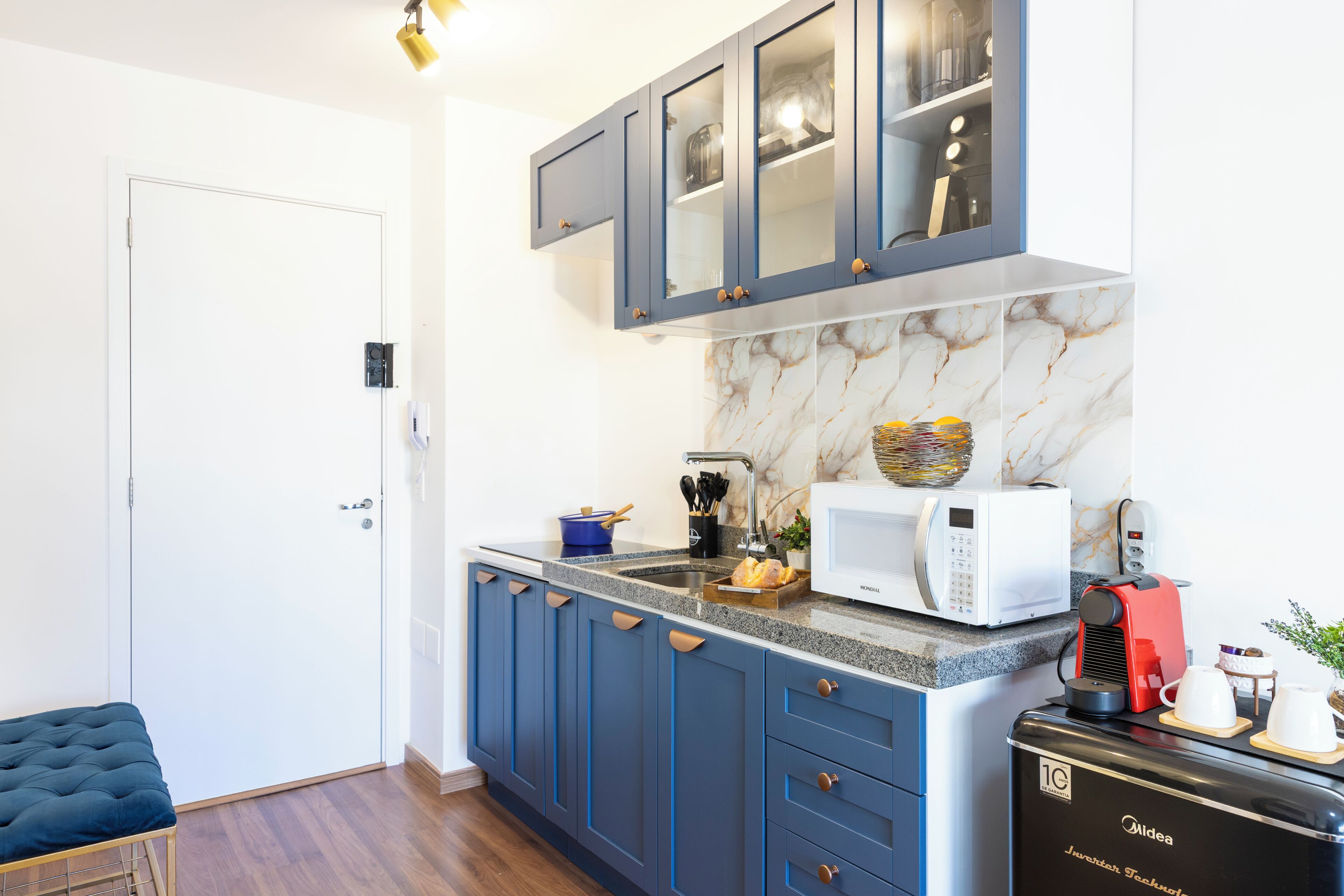 A modern kitchen with blue cabinets, a white microwave, and a red coffee machine.