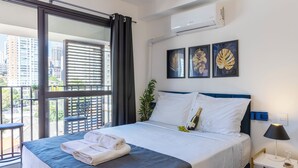 Habitación de hotel con cama, mesita de noche, lámpara, ventana con cortinas y una obra de arte en la pared.