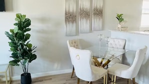Un coin repas avec une table en verre, des chaises à revêtement blanc et une plante en pot.