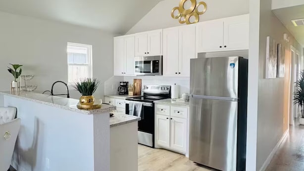 Une cuisine moderne avec des meubles blancs, des appareils en acier inoxydable et un plancher en bois.