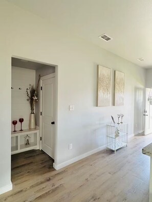 A hallway with a white door, a small shelf with decorative items, and two wall-mounted artworks.