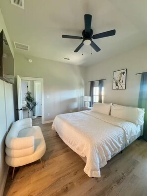 Un dormitorio con cama, ventilador de techo, planta en maceta y una silla.