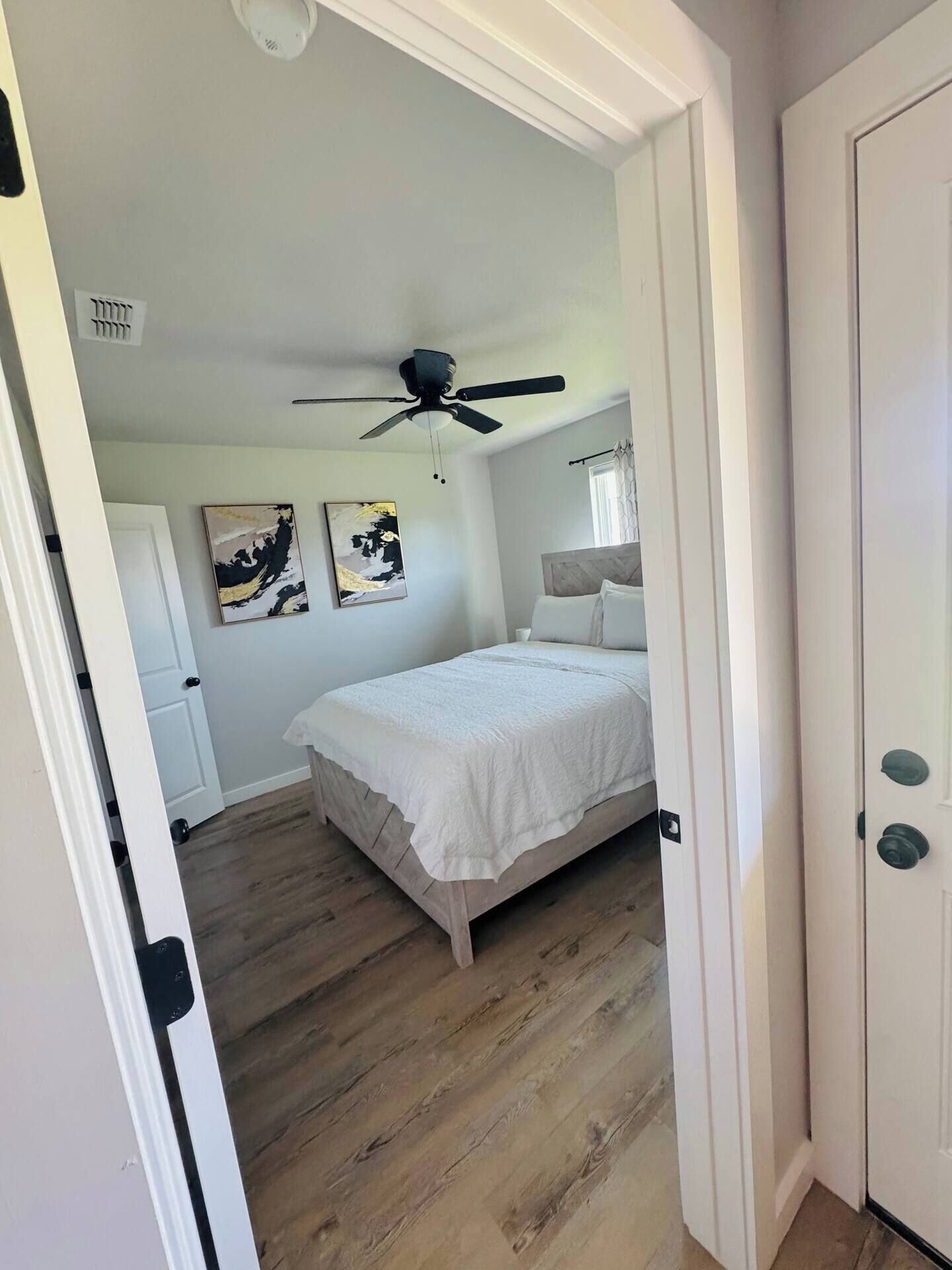 A bedroom with a bed, a ceiling fan, and two abstract paintings on the wall.