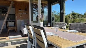 An outdoor dining area with a wooden table, white chairs, and a glass door leading to a kitchen. - 4 Star Holiday Home in Sydals (Sydals)