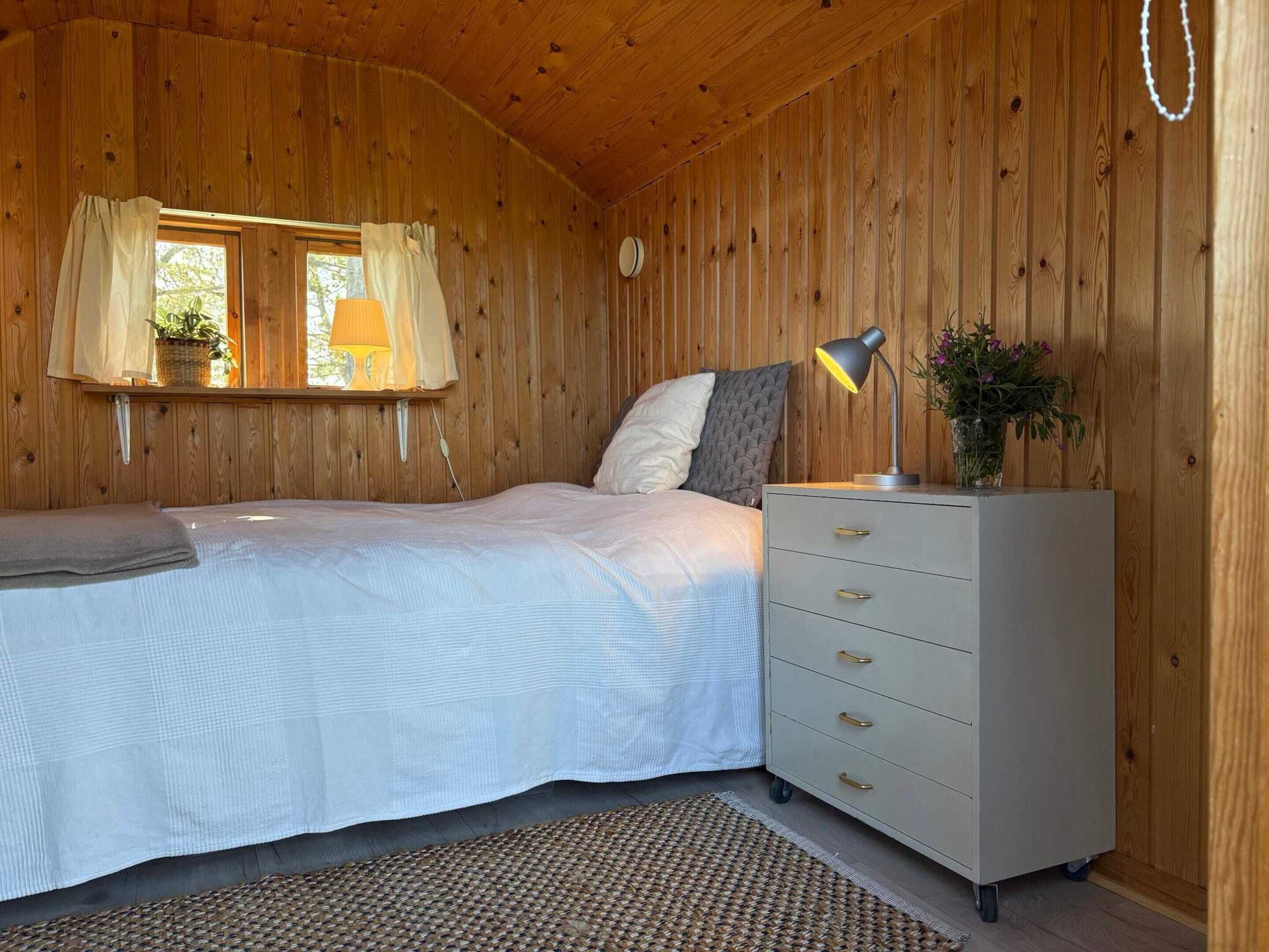 A wooden room with a bed, a dresser, a lamp, and a window with curtains.