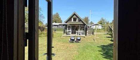 A view through a wooden door of a house with a lawn, outdoor seating, and a swing set.