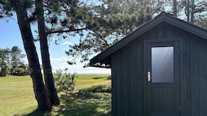 A small, dark wooden shed with a white base, surrounded by grass and trees. - 4 Star Holiday Home in Sydals (Sydals)