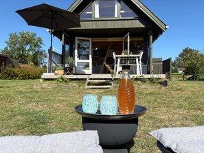 Une maison moderne dotée d’une terrasse, d’une table de patio avec une bouteille et des verres, et d’une pelouse.