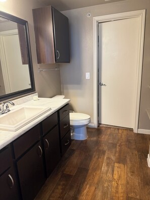 A bathroom with a white sink, dark wooden cabinets, a white toilet, and a wooden floor.
