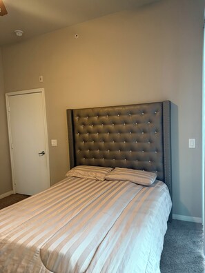 A bedroom with a tufted headboard, a striped bedspread, and a door.
