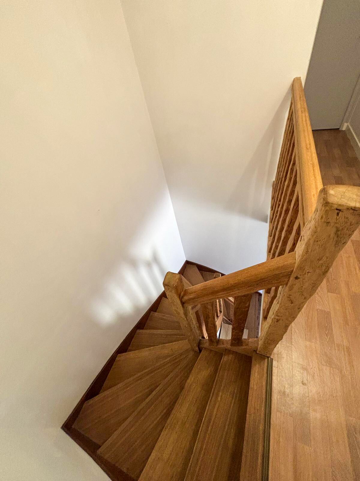 Un escalier en bois, doté d’une rampe, mène à un palier dont le sol est également en bois.
