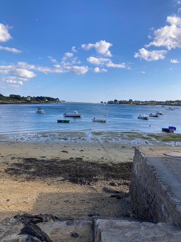 A coastal scene with boats on calm water, a sandy beach, and a stone wall in the foreground. - Renovated farmhouse dating from 1821 (SAINTE HELENE)