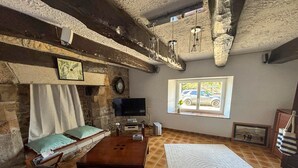 Ein gemütliches Wohnzimmer mit Kamin aus Stein, Fernseher, großem Fenster mit Blick auf parkende Autos und einer Couch.