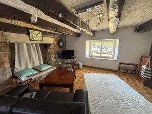 A cozy living room with a stone fireplace, a television, a large window with a view of parked cars, and a sofa. - Renovated farmhouse dating from 1821 (SAINTE HELENE)