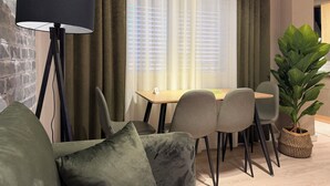 A modern living room with a sofa, a dining table with chairs, a floor lamp, and a large plant. - Perla Cozy Apartment (Scutari)