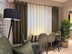 A modern living room with a sofa, a dining table with chairs, a floor lamp, and a large plant.