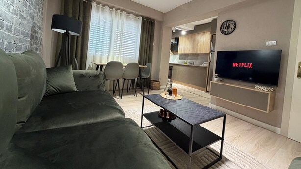A modern living room with a sofa, a coffee table, a TV, and a kitchen area in the background. - Perla Cozy Apartment (Scutari)