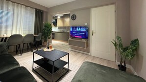 A modern living room with a sofa, a coffee table, a TV, and a dining area with chairs and a table. - Perla Cozy Apartment (Scutari)