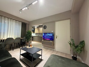 A modern living room with a sofa, a coffee table, a TV, and a dining area with chairs and a table.