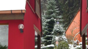 Uma trilha coberta de neve que leva a um prédio vermelho com uma janela e um candeeiro fixado na parede.