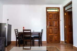 A dining area with a table and chairs, a wooden door, and a refrigerator. - Karen Brooks View Palace- 2 Bedroom (Nairobi)
