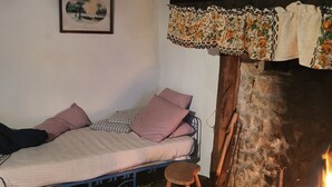 Una habitación rústica con una cama, un taburete de madera, una chimenea y un cuadro enmarcado en la pared.