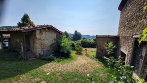 Un patio rústico con edificios de piedra, un área con césped y una silla roja.