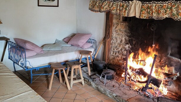 Una habitación rústica con una cama, un taburete pequeño, una chimenea y un cuadro en la pared.