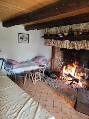 A rustic room with a bed, a small stool, a fireplace, and a framed picture on the wall.