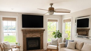 Una sala de estar con chimenea, ventilador de techo y un ventanal grande.
