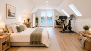 Un dormitorio con cama, escritorio, bicicleta estática y vista hacia un cuerpo de agua a través de una puerta de cristal.