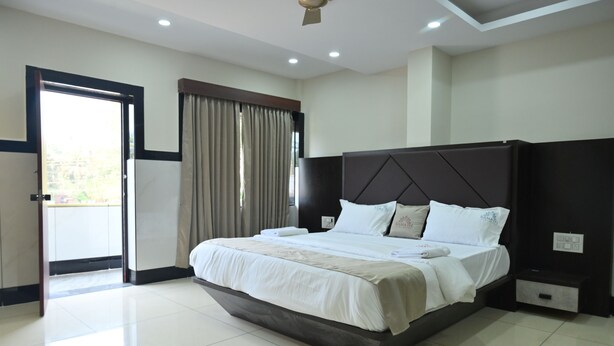 A modern hotel room with a large bed, a ceiling fan, and a view through an open door. - Kamath Yatri Nivas Plus (Bhatkal)