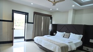 A hotel room with a large bed, a ceiling fan, a wardrobe, and a door leading to a balcony. - Kamath Yatri Nivas Plus (Bhatkal)