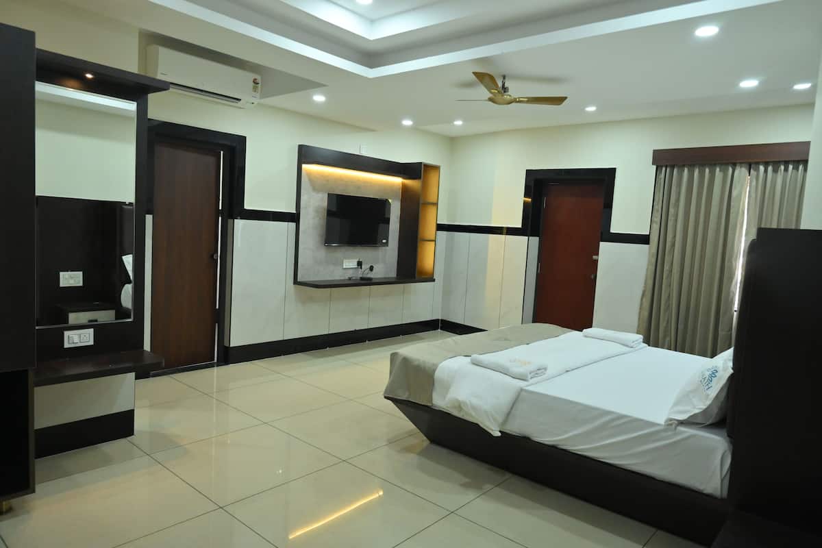 Una habitación de hotel con una cama, un televisor montado en la pared, un ventilador de techo y una ventana con cortinas.