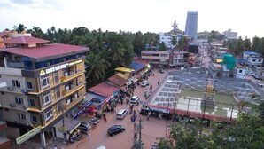 A multi-story hotel with balconies, a parking area, and a temple complex in the background. - Kamath Yatri Nivas Plus (Bhatkal)