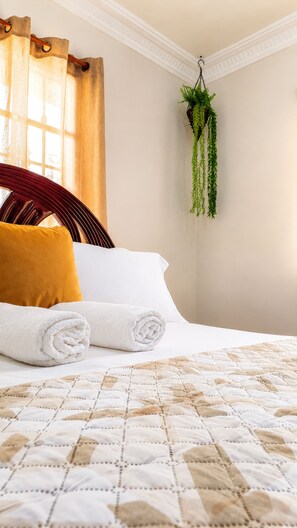 A neatly made bed with rolled white towels, a patterned quilt, and a yellow pillow.