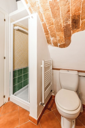 Kylpyhuone, jossa on wc, suihku ja laatoitettu lattia.