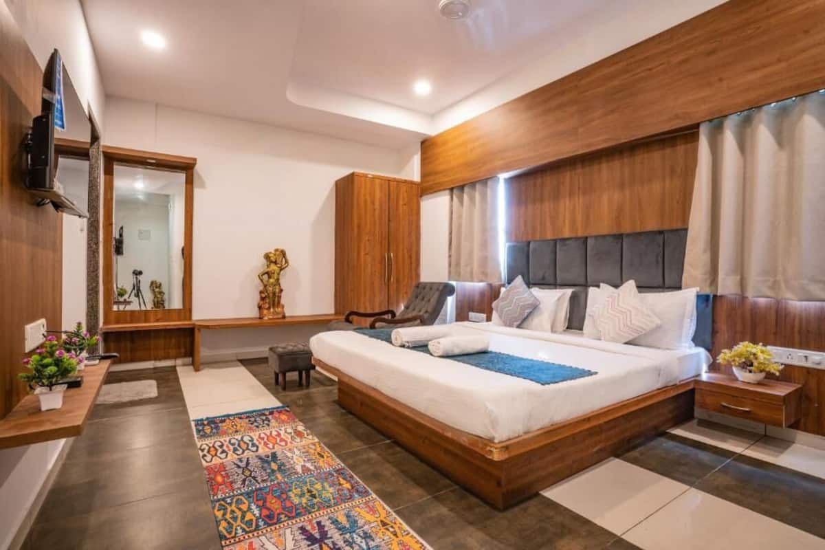 A bedroom with a large bed, a wooden headboard, a television, a desk with a computer, and a mirror.