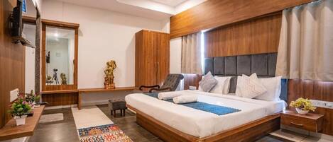 A bedroom with a large bed, a wooden headboard, a television, a desk with a computer, and a mirror.