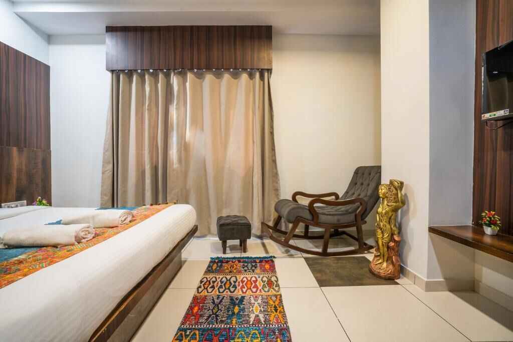 Une chambre d’hôtel avec un lit, un petit tabouret, un fauteuil à bascule, une statue décorative et un téléviseur fixé au mur.
