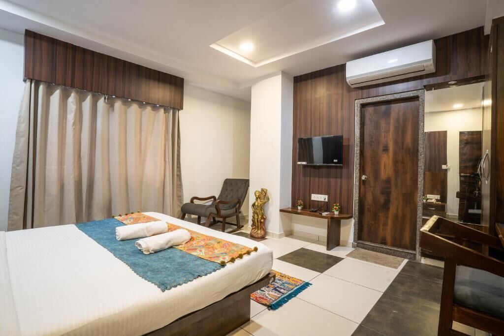 Een hotelkamer met een bed, een stoel, een televisie, een kledingkast en een airconditioning.